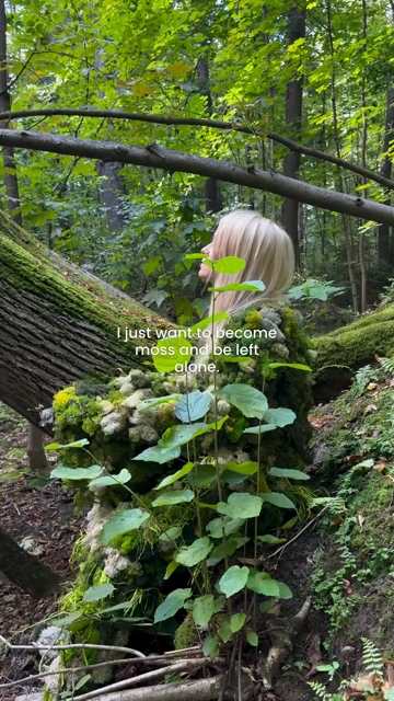 A woman dressed perfectly in moss lies down in the forest, becoming one with it